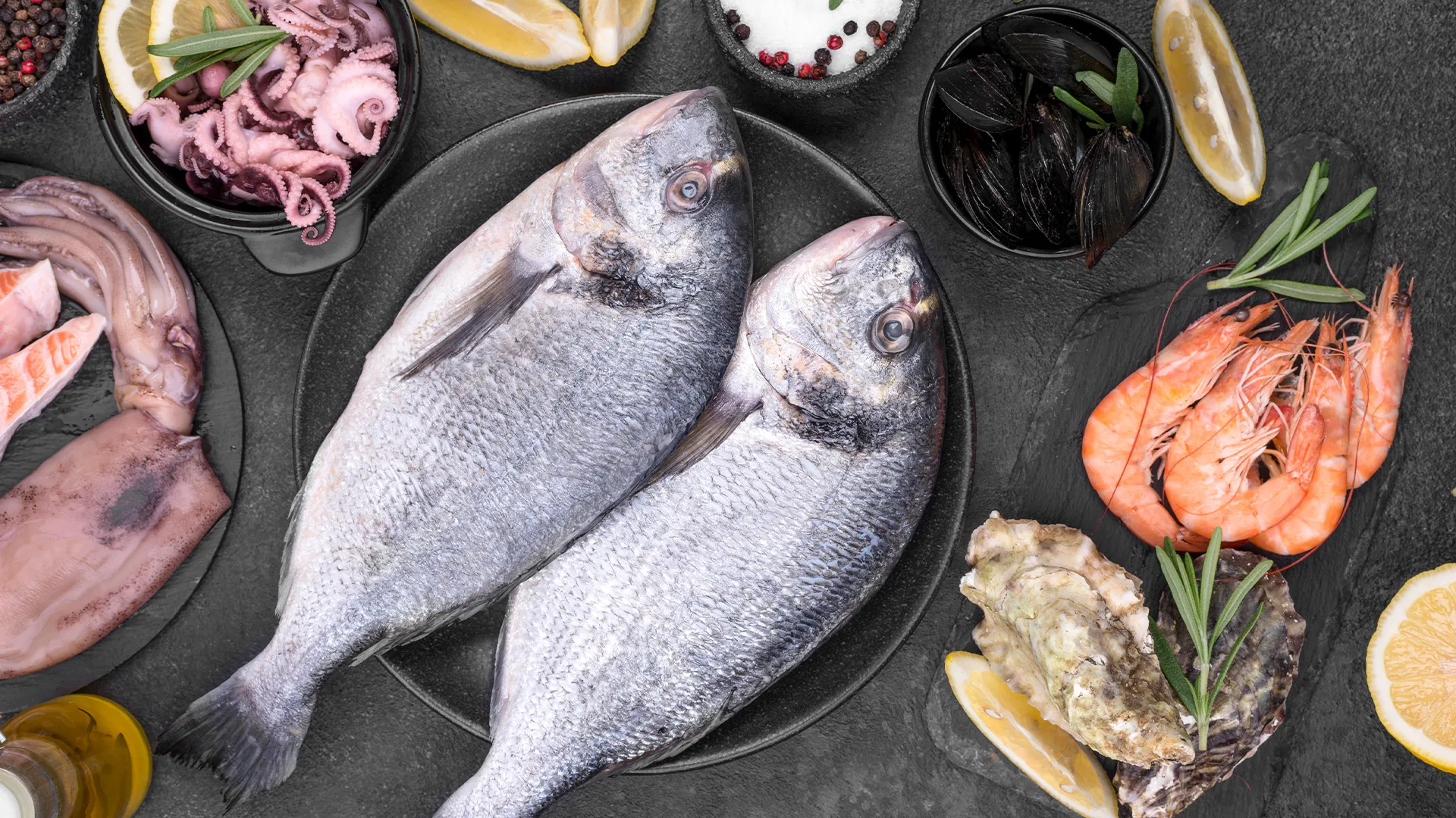 Overhead flat-lay of fresh tuna, shrimp, oysters, mussels, and salmon on a dark surface